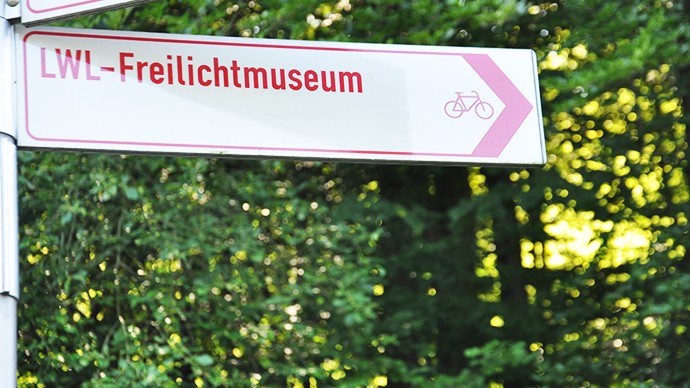 Ein Schild vom Radverkehrsnetz, das den Weg zum Museum weist. Auf dem Schild ist die Aufschrift LWL-Freilichtmuseum mit einem Fahrradsymbol. Ein Schild vom Radverkehrsnetz, das den Weg zum Museum weist. Auf dem Schild ist die Aufschrift LWL-Freilichtmuseum mit einem Fahrradsymbol.