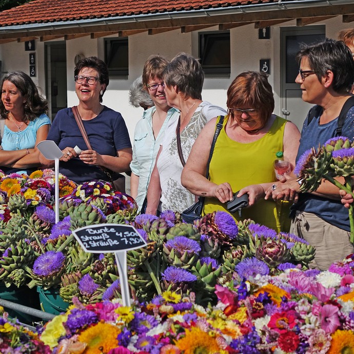 An einem Stand mit bunten Sträußen aus Herbstblumen stehen neun Frauen, die Blumen kaufen möchten. (öffnet vergrößerte Bildansicht)