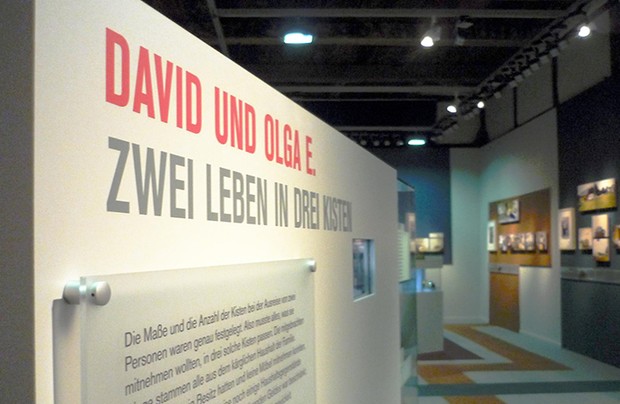 Eine Wand unserer Ausstellung mit dem Text "David un Olga E. Zwei Leben in drei Kisten"