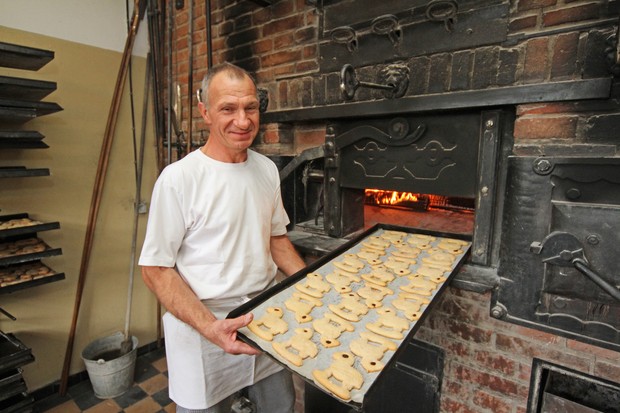 Ein Bäcker steht mit einem Backblech voller Kekse an einem aus Stein gemauerten Backofen.