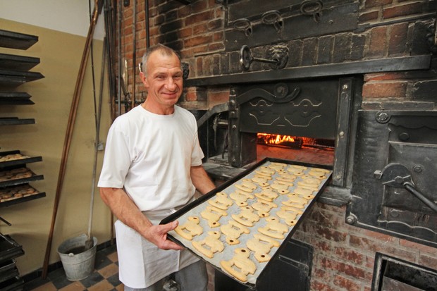 Ein Bäcker steht mit einem Backblech voller Kekse an einem aus Stein gemauerten Backofen. Ein Bäcker steht mit einem Backblech voller Kekse an einem aus Stein gemauerten Backofen.
