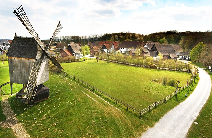 Vordergrund eine historische Windmühle. Rechts ist ein Weg zum Paderborner Dorf. Das Paderborner Dorf ist im Hintergrund.