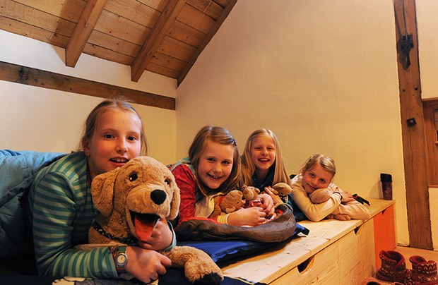 Vier Mädchen, die im Schlafsaal von Hof Remberg auf ihren Schlafmatten liegen. Sie haben Kuscheltiere dabei.