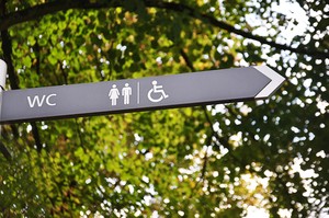 Ein Schild mit Symbolen darauf. DIe Symbole und der Pfeil auf dem Schild weisen den Weg zu den Toiletten und Behindertentoiletten.