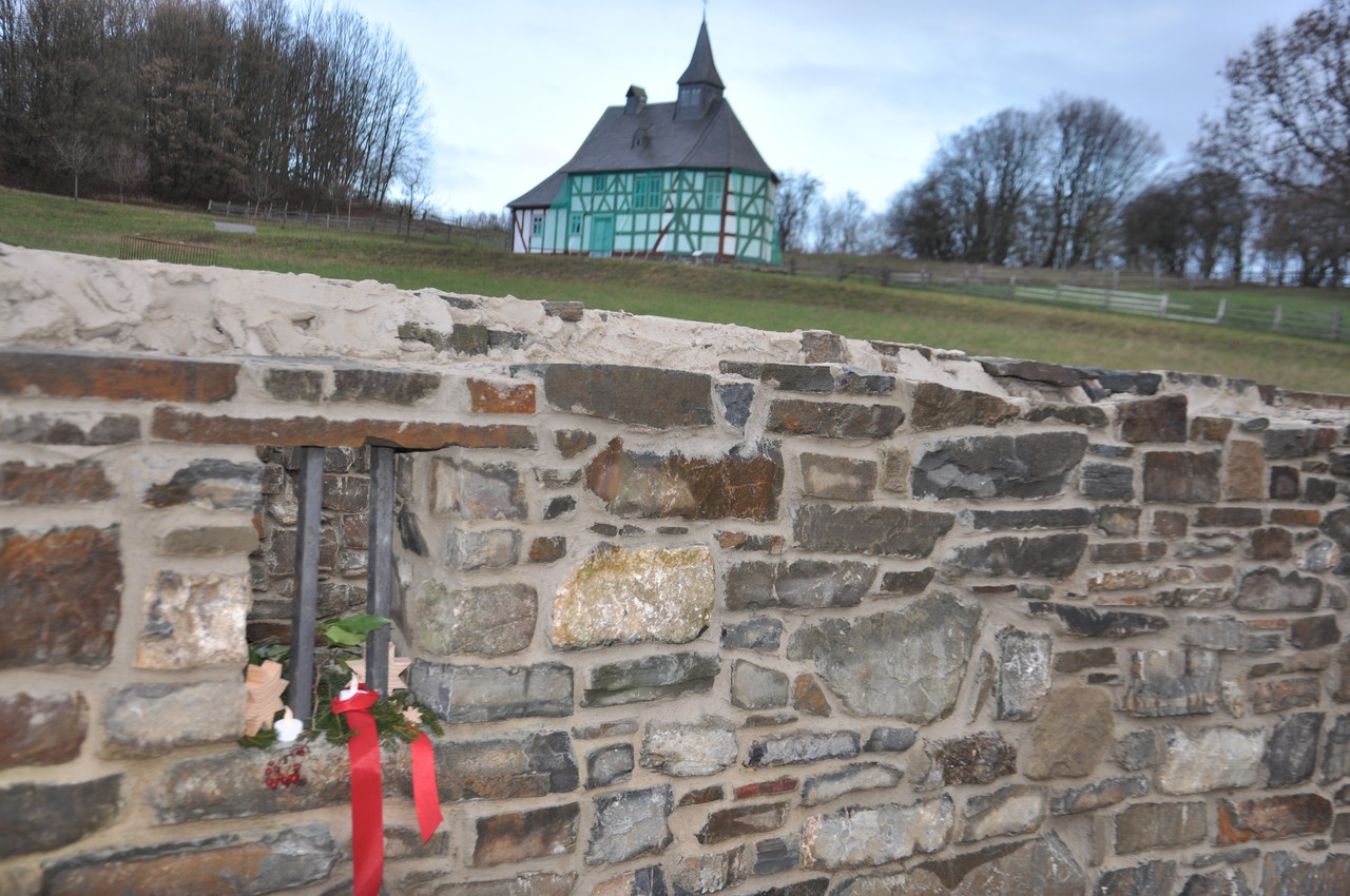 Ein Kellerfenster ist mit einer roten Schleife und einem Tannenzweig geschmückt.