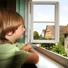 Einen Jungen, der aus einem Fenster schaut. Hinter dem Fenster sind Häuser des Museums.
