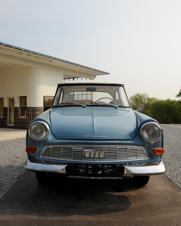 Forntanischt eines blauen DKW. Im Hintergrund sind die Umrisse einer Tankstelle erkennbar.