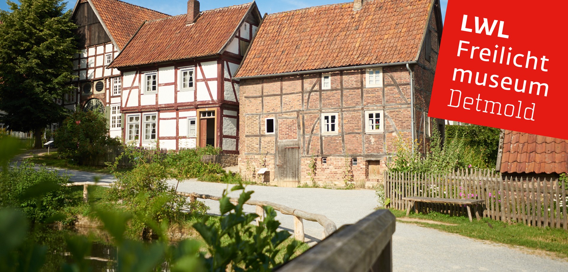 Zwei Gebäude im Paderborner Dorf. Links der Teich. Mittig der Fußweg.